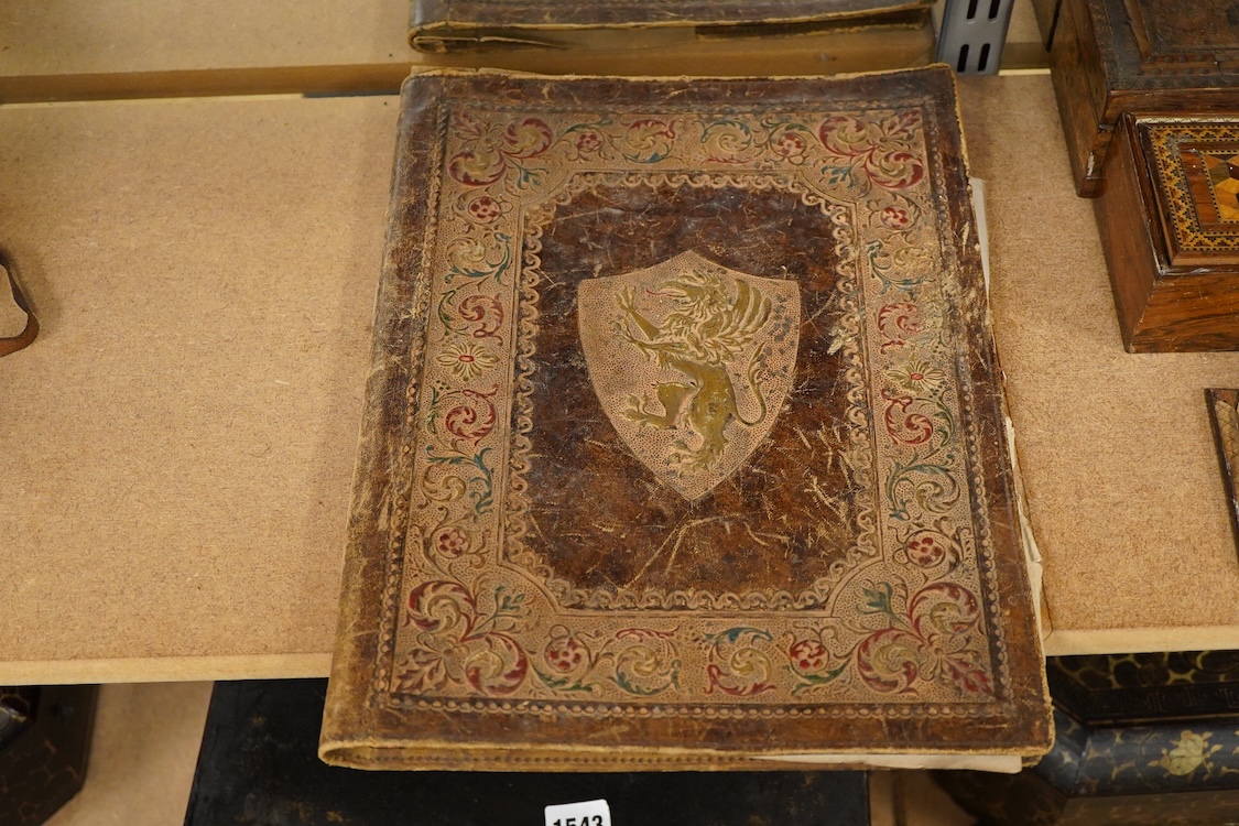 Two gilt metal plaques housed in giltwood ‘cherub’ frames and a heraldic leather folder with watered silk lining, 34 x 27cm